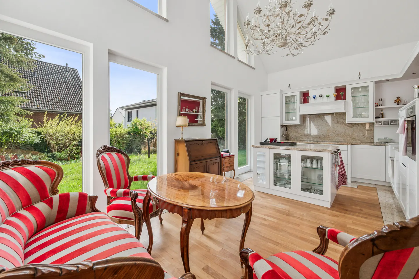 Bright open-plan kitchen and living area with red and white striped vintage chairs, a wooden table, and a crystal chandelier.