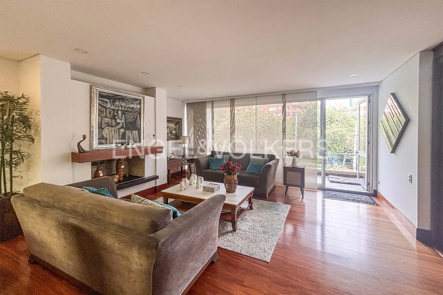 Living room with brown sofas, a fireplace, and a marble coffee table on a patterned rug. Sliding glass doors lead to a balcony.