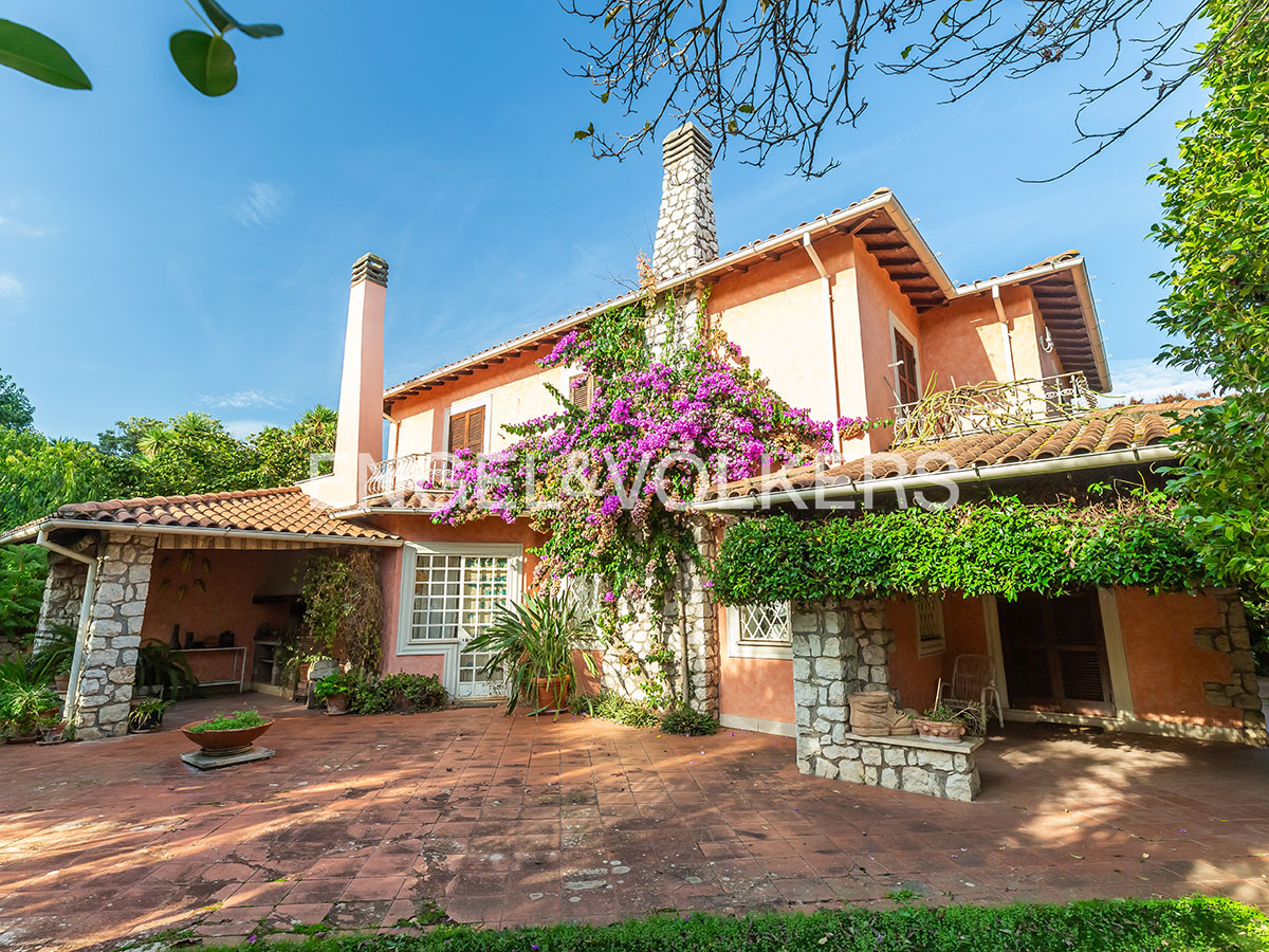Peach-colored two-story villa with stone chimneys, a tiled patio, and vibrant purple bougainvillea against a blue sky. [AI-generated text]