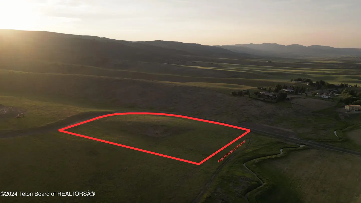 Aerial view of a green field outlined in red, with mountains in the background at sunset.