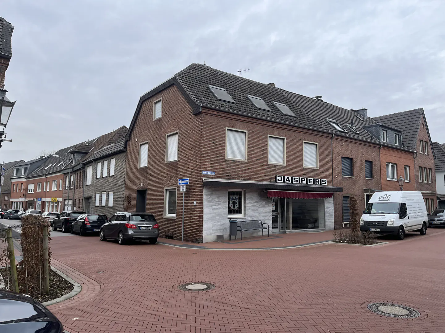 Street view of a two-story brick building with "JASPERS" sign above the storefront. Cars parked along the street. Cloudy sky.