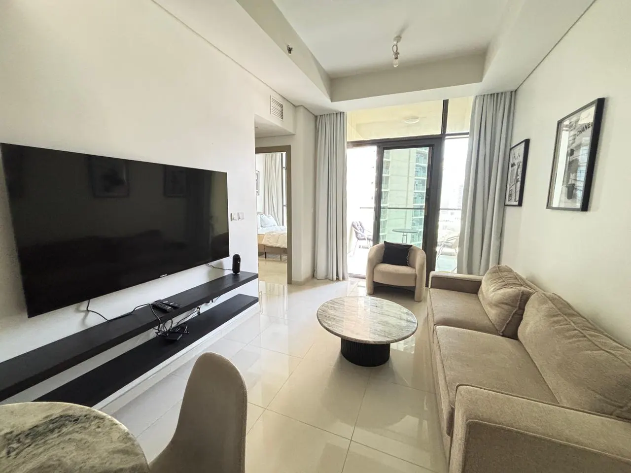 Living room with beige sofa, round marble table, TV, and balcony with city view.