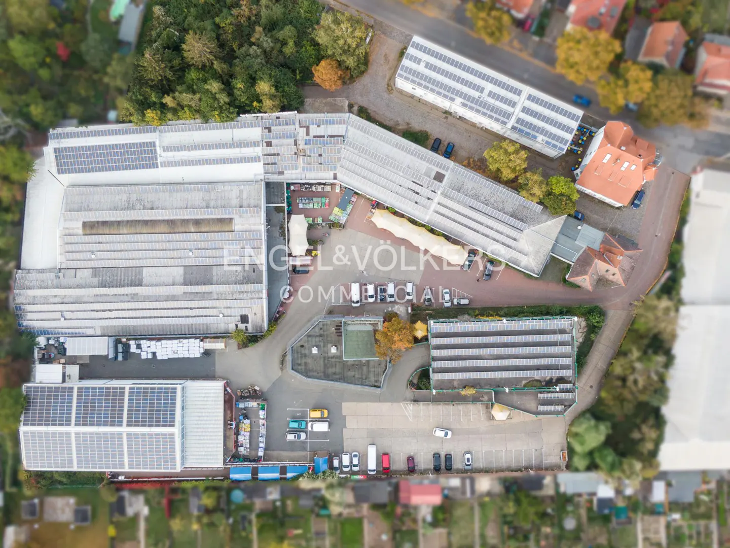 Aerial view of a commercial complex with multiple buildings featuring solar panels, parking areas, and surrounding trees.