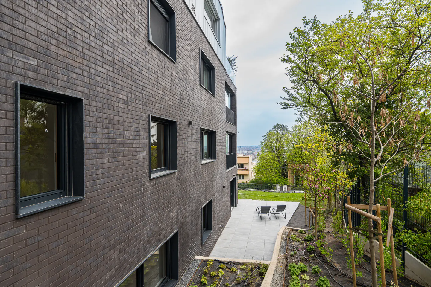 Exterior of a modern brick apartment building with a patio and garden area.