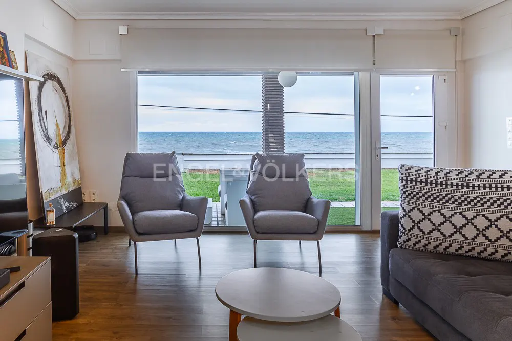 Living room with two gray armchairs facing a large window with ocean view. A gray sofa with patterned pillow is on the right.