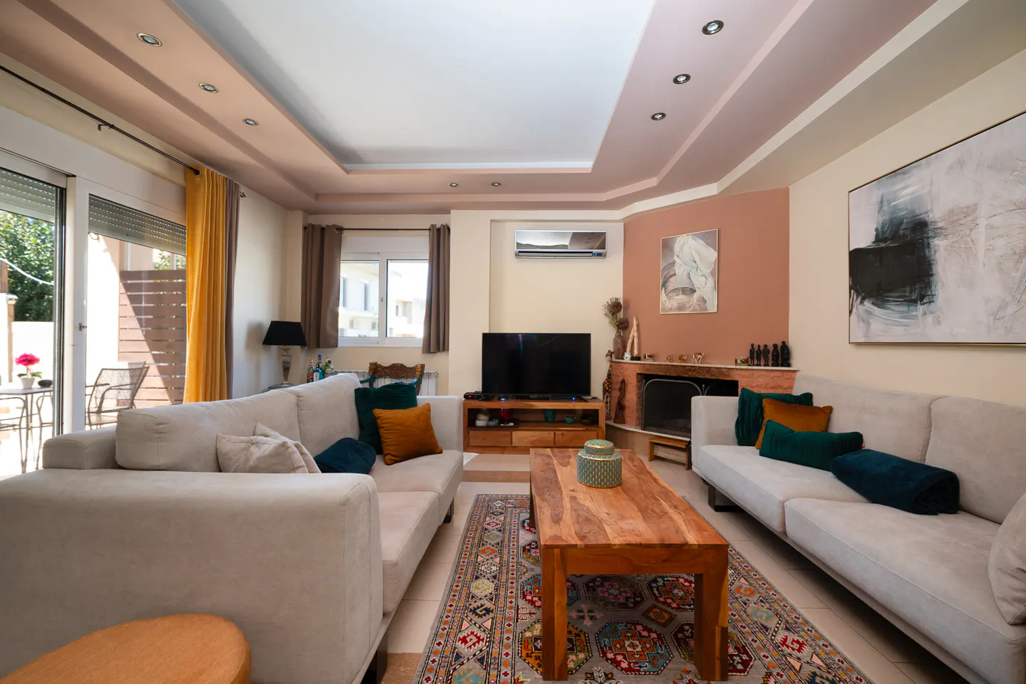 Living room with beige sofas, a wooden coffee table on a patterned rug, and a TV above a wooden console.