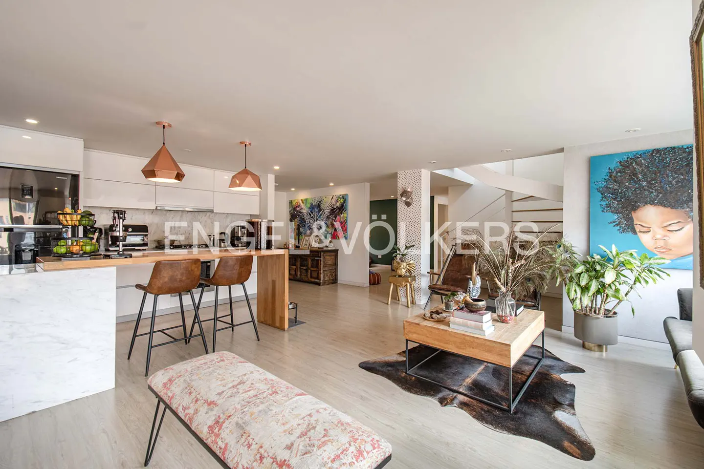 Open-concept living space with a kitchen island, leather bar stools, and a wooden coffee table on a cowhide rug. A large painting hangs on the wall.