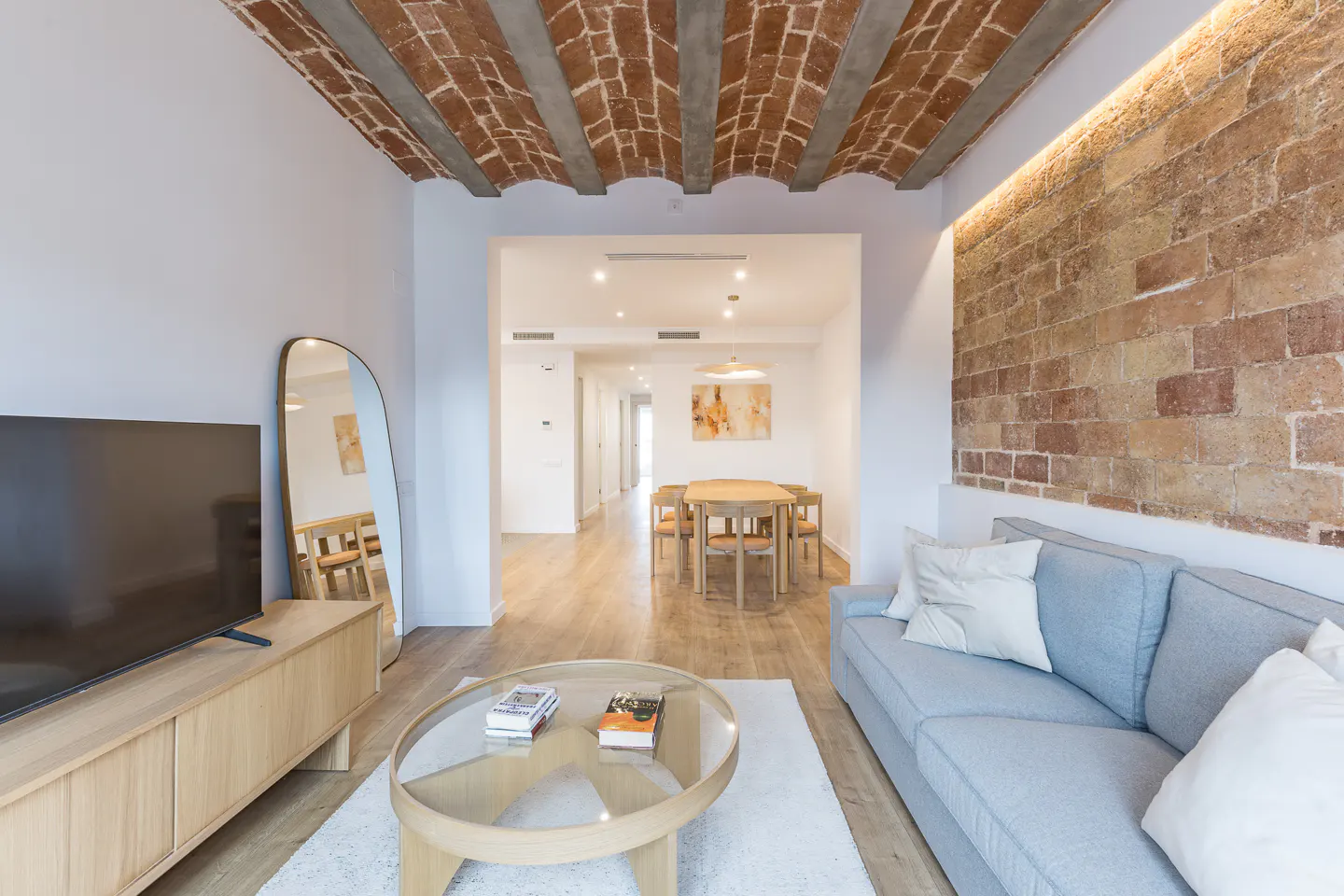 Living room with brick ceiling and wall, light blue sofa, wood floors, and dining area in the background.