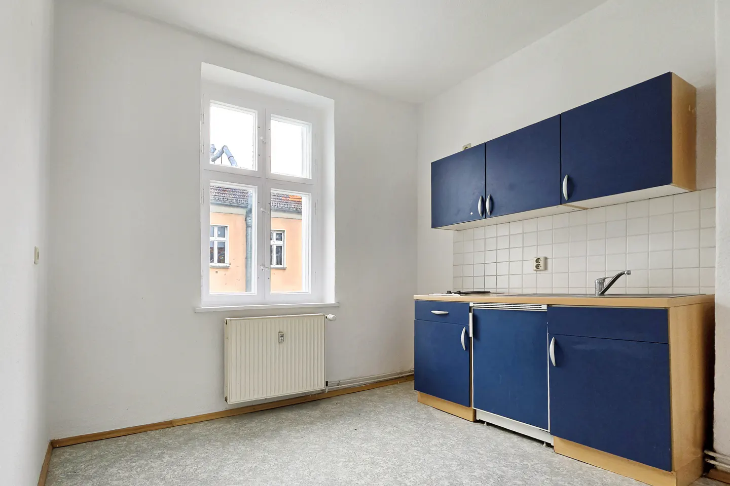 Bright kitchen with white walls, blue cabinets, and a window showing a building outside.
