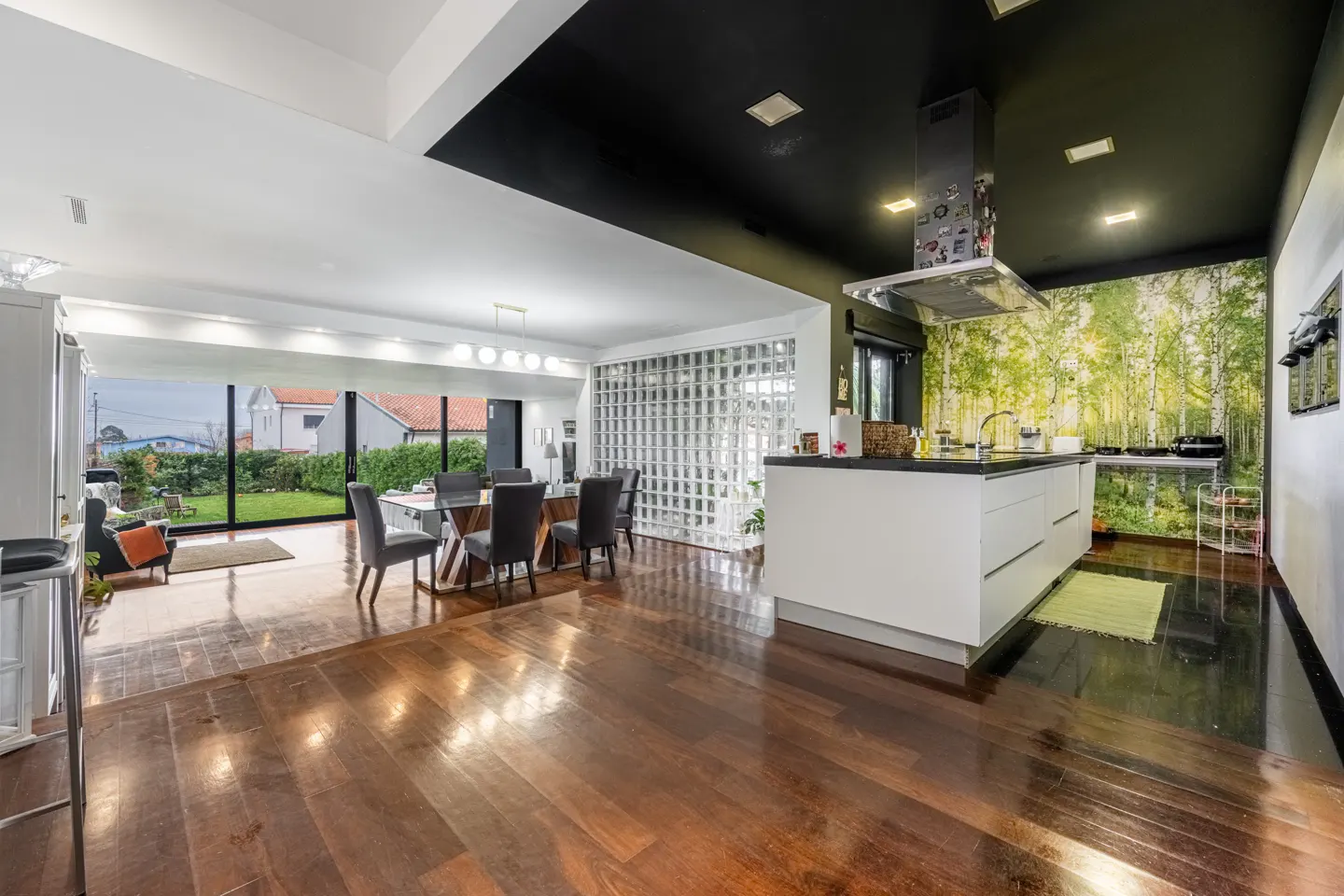 Modern open-plan kitchen and dining area with hardwood floors, a black ceiling, and a forest-themed mural wall.