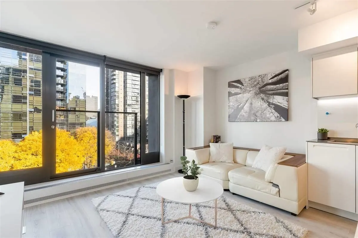 Bright, modern apartment living room with a white sofa, round table, and city view through large windows.