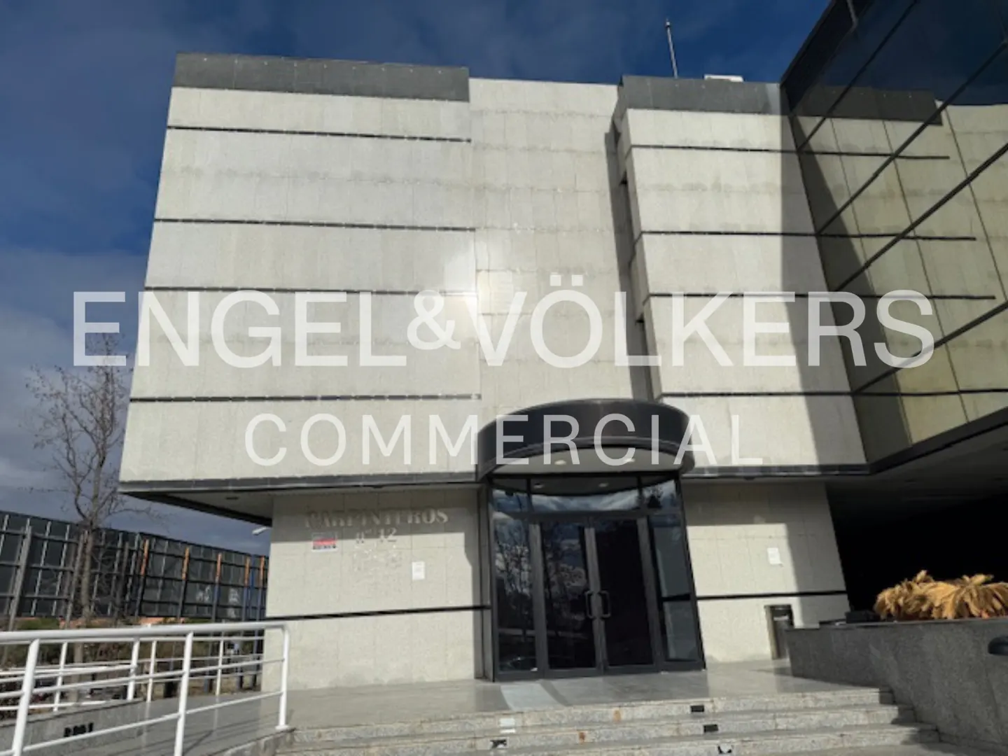 Exterior of an Engel & Völkers Commercial building with a revolving door entrance and gray stone facade.