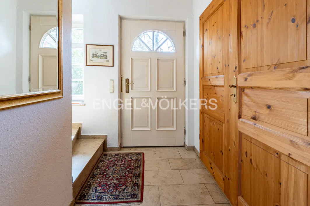 Entryway with beige tile floor, a red patterned rug, a white front door with a half-moon window, and a light wood paneled door.
