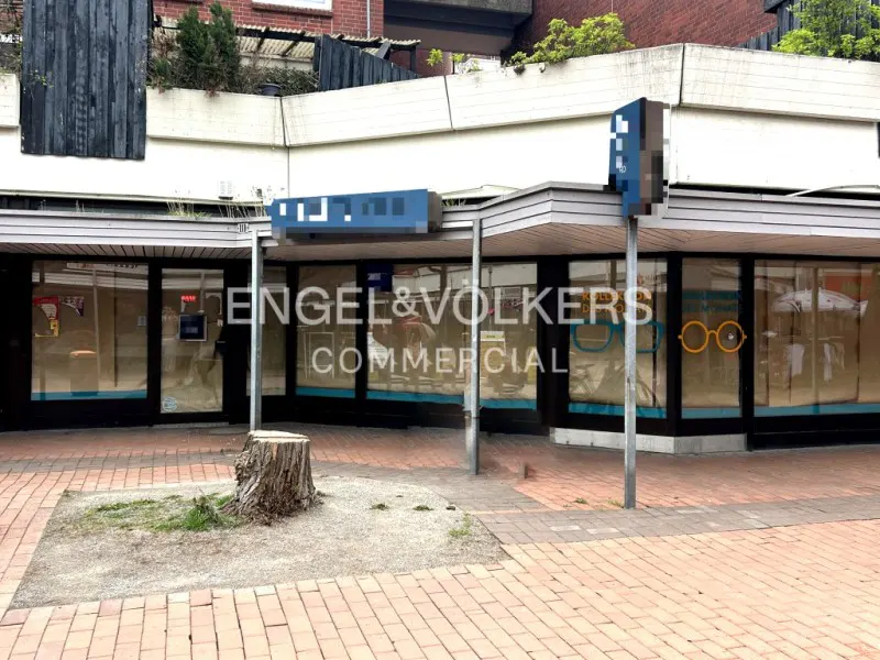 Exterior view of an Engel & Volkers Commercial storefront with large windows and a brick walkway. A tree stump sits in front.