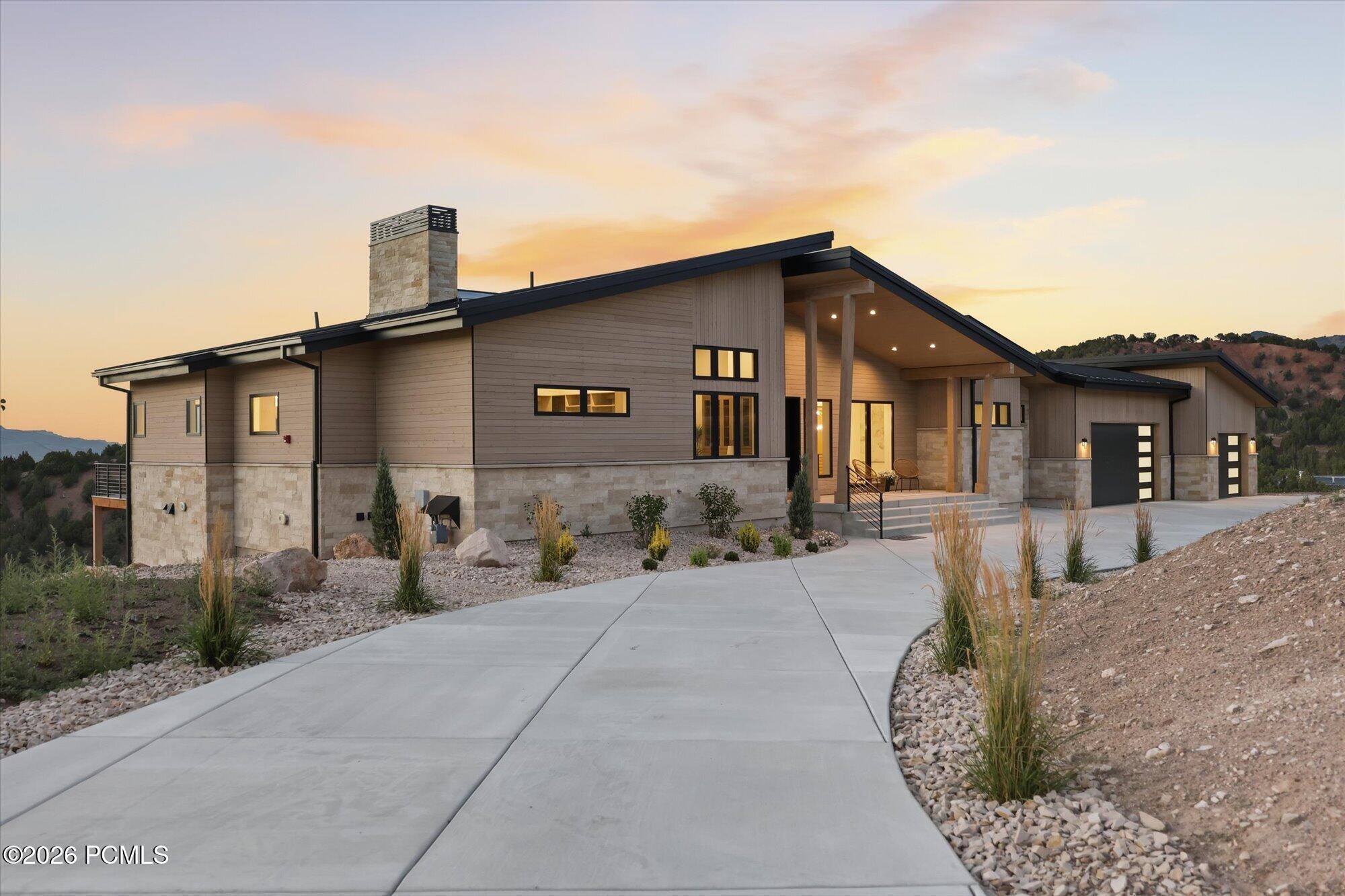 Modern home with wood and stone siding, a concrete driveway, and a sunset sky in a mountainous landscape.