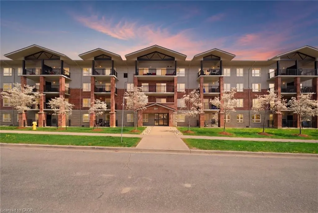 Three-story apartment building with balconies, brick pillars, and gray siding under a pink and blue sky.