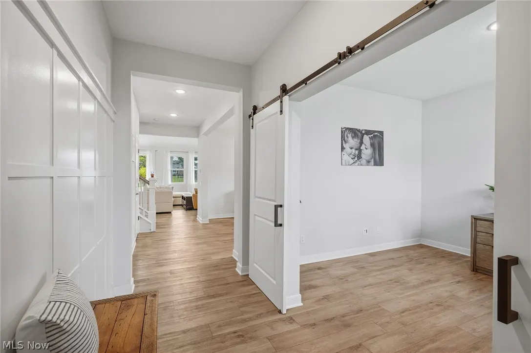 Bright, modern home interior with wood floors, white walls, and a sliding barn door. A hallway leads to a living area with natural light.