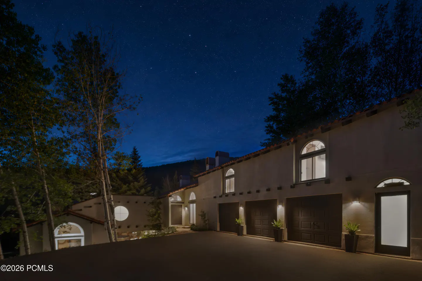 Exterior of a stucco home at night with a three-car garage, illuminated windows, and a starry sky above.