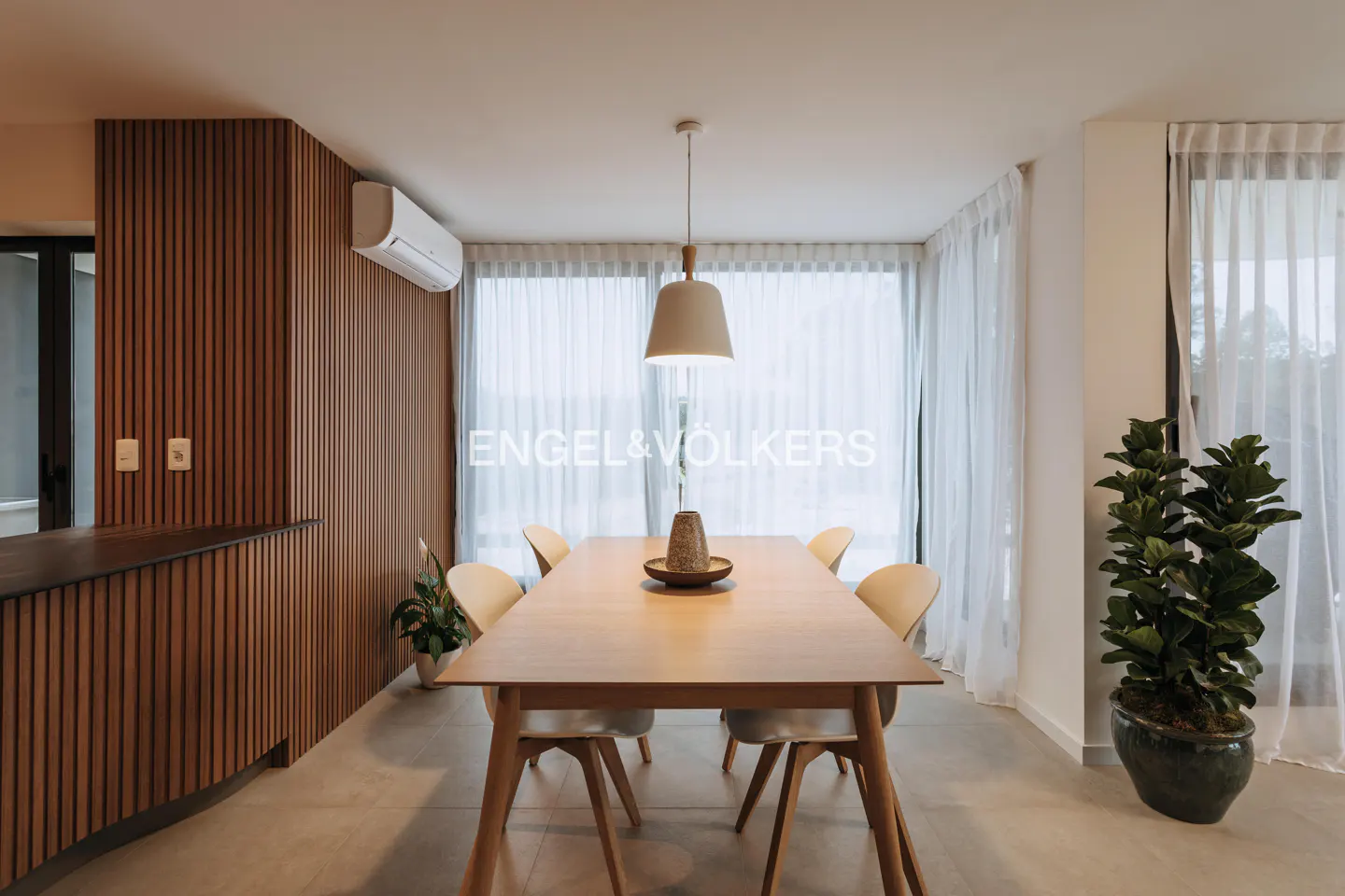 Bright dining room with wood table, chairs, and accent wall. A pendant light hangs above the table. Sheer curtains cover the windows.