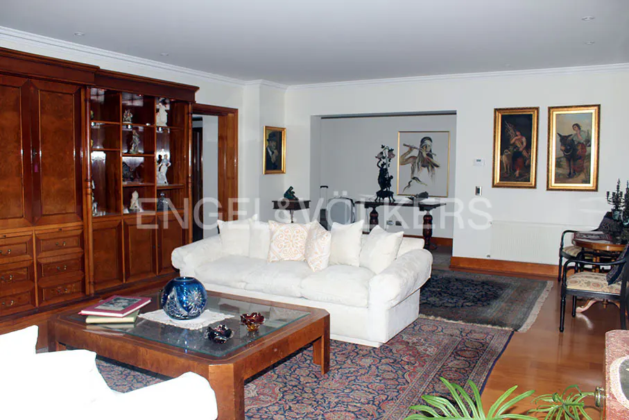 Living room with a white sofa, wood furniture, and framed art on the walls. A patterned rug covers the wood floor.