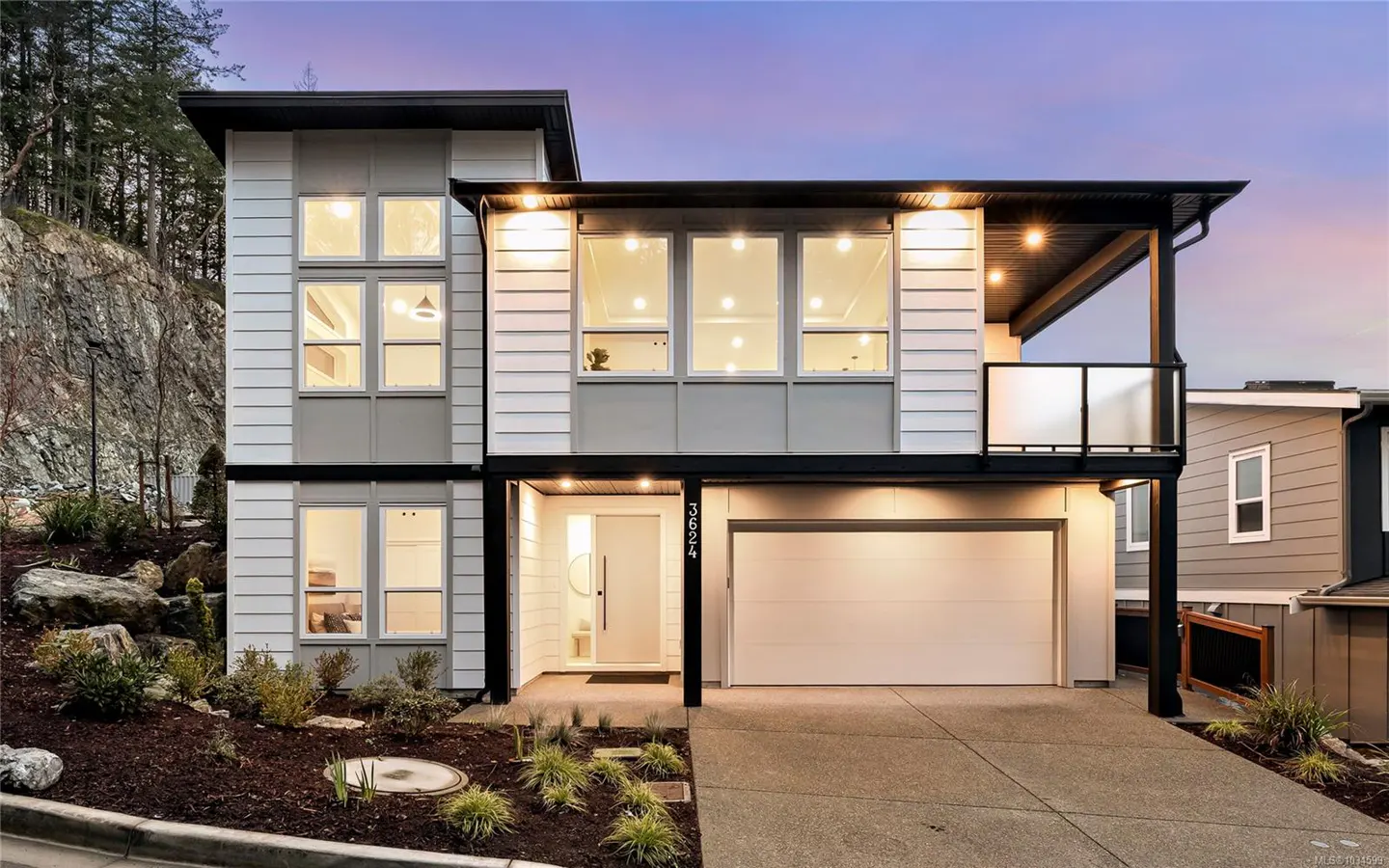Two-story modern home with white siding, gray accents, and black trim. Large windows glow with interior light. Landscaped yard and driveway in front.
