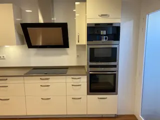 Modern kitchen with cream cabinets, black induction cooktop, angled range hood, and a built-in coffee machine and oven stack.