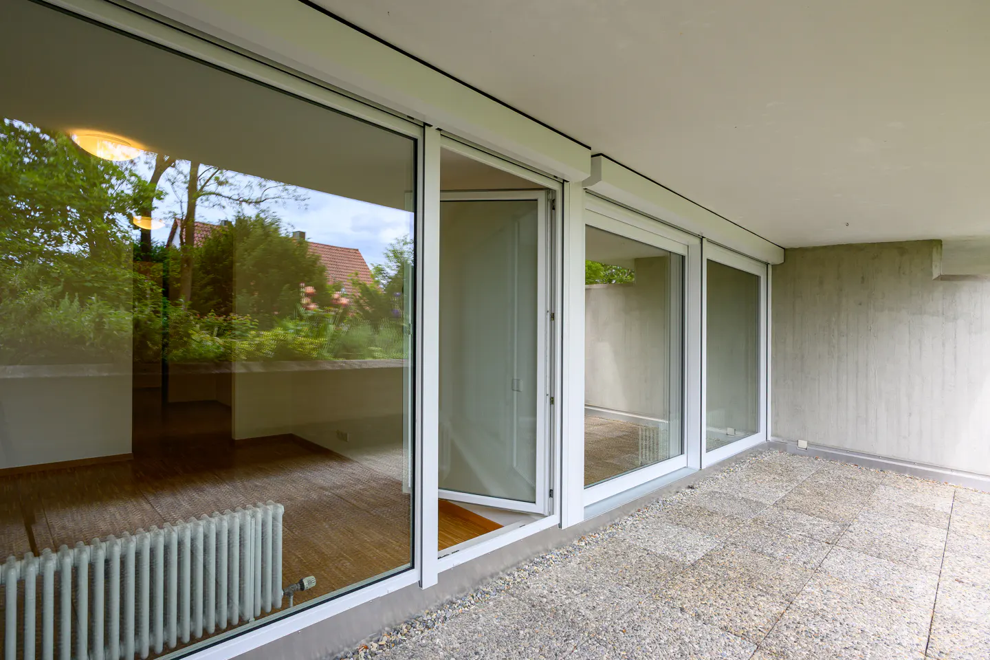 Patio with stone tiles and white framed glass doors. One door is open, reflecting a radiator and trees.