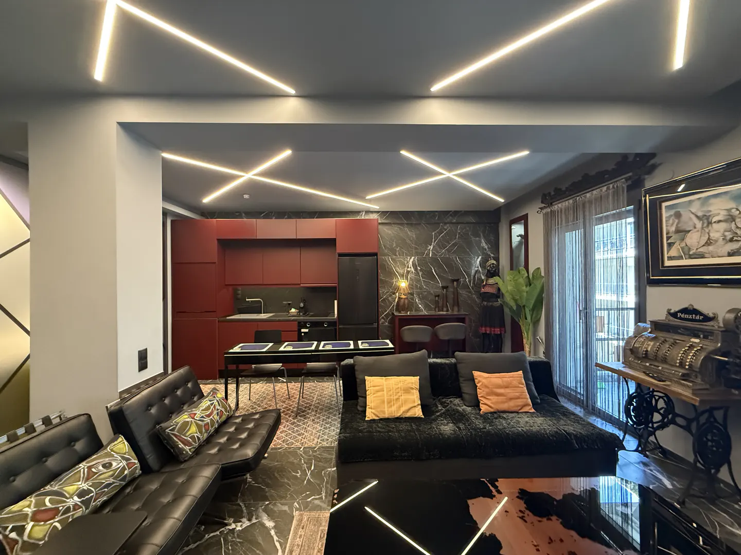 Open-concept apartment with black marble floors, red kitchen cabinets, and modern lighting. A black sofa with yellow pillows sits in the living area.