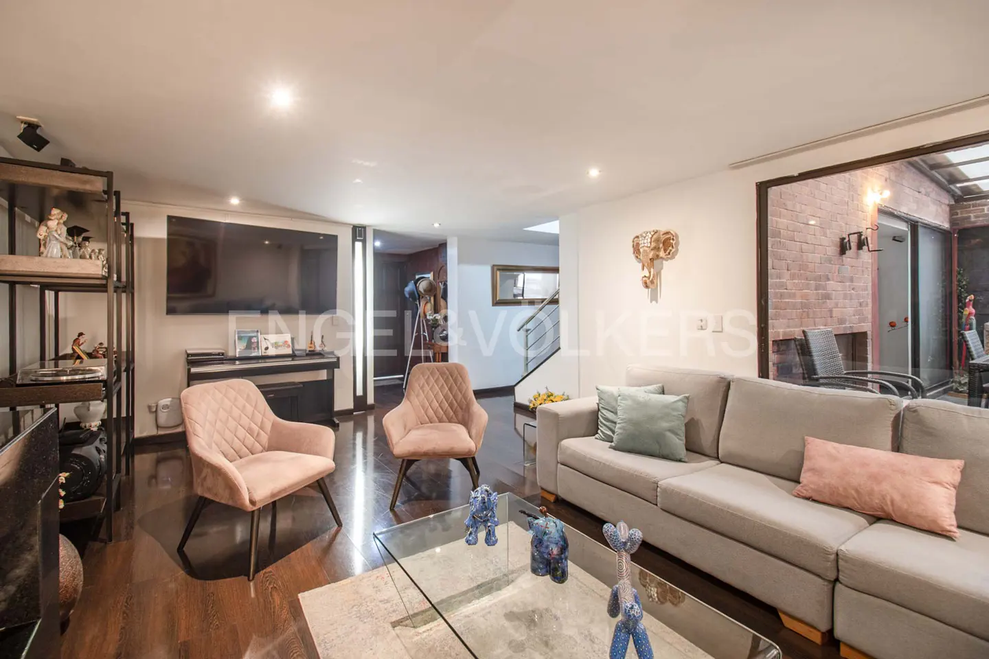 Living room with hardwood floors, a gray sofa with pillows, two pink chairs, and a glass coffee table with blue figurines.