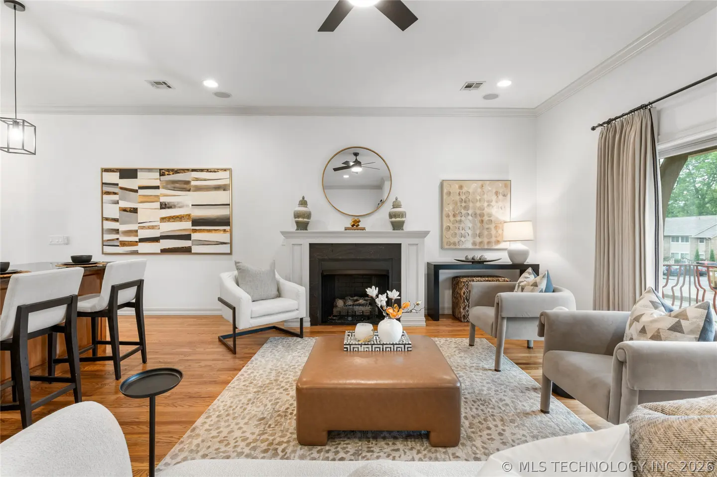 Living room with white walls, hardwood floors, and a fireplace. There are two gray chairs, a brown ottoman, and a bar with stools.