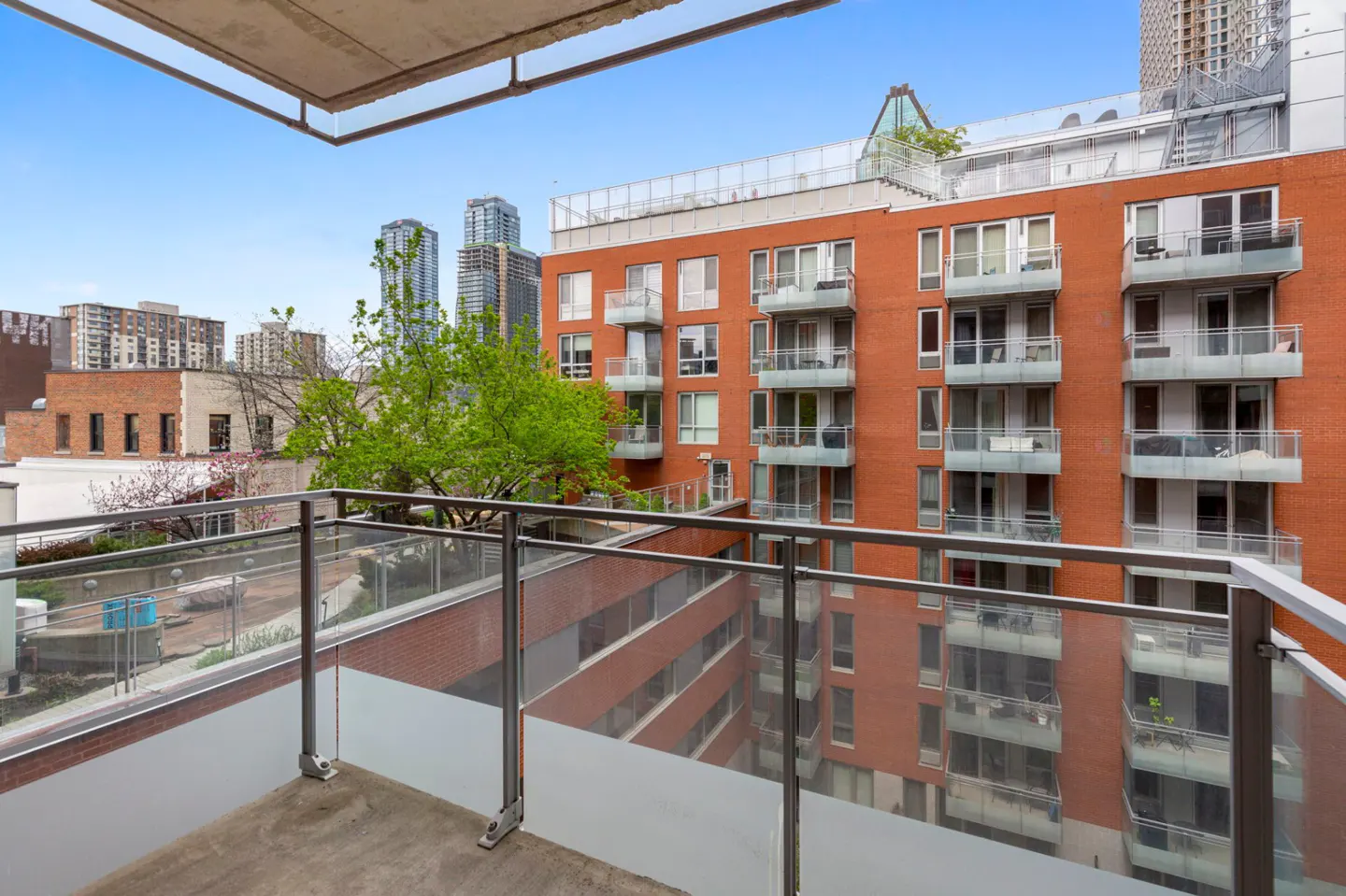 View from a balcony overlooking a red brick apartment building with glass railings and city skyscrapers in the background.