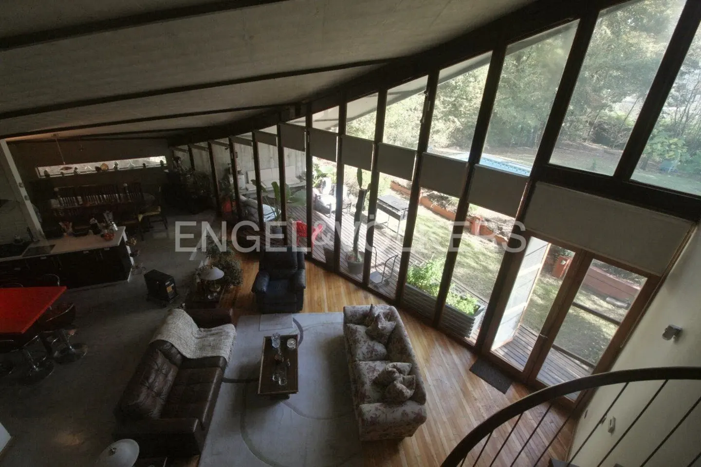 Aerial view of a living room with sofas, a coffee table, and floor-to-ceiling windows overlooking a garden with a pool.