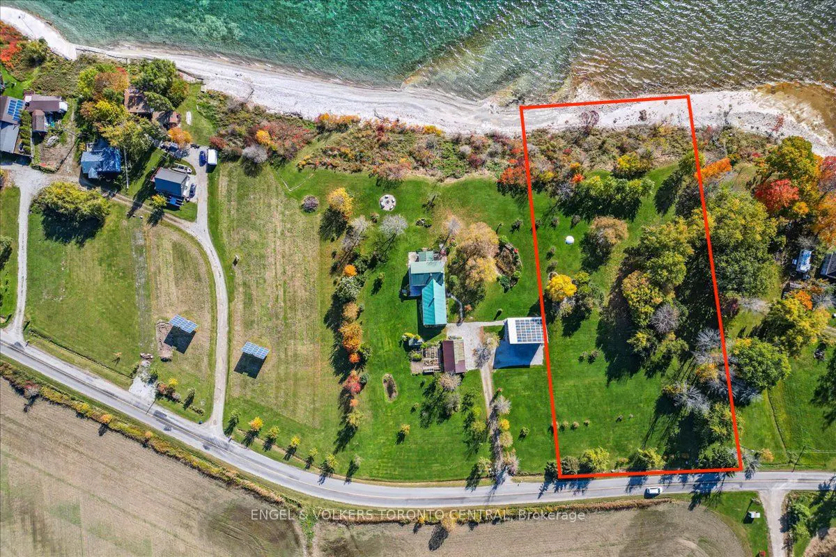 Aerial view of a property with a green lawn, trees, and a house with a green roof, bordered by a red line, next to a beach and turquoise water.