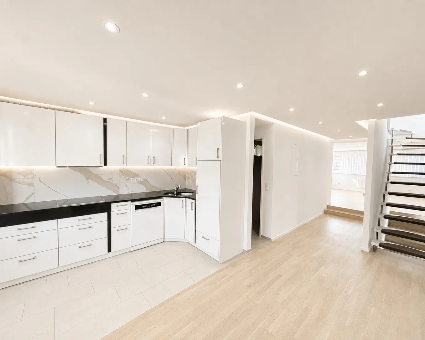 Bright, modern kitchen with white cabinets, black countertops, and marble backsplash. Wood floors lead to stairs.