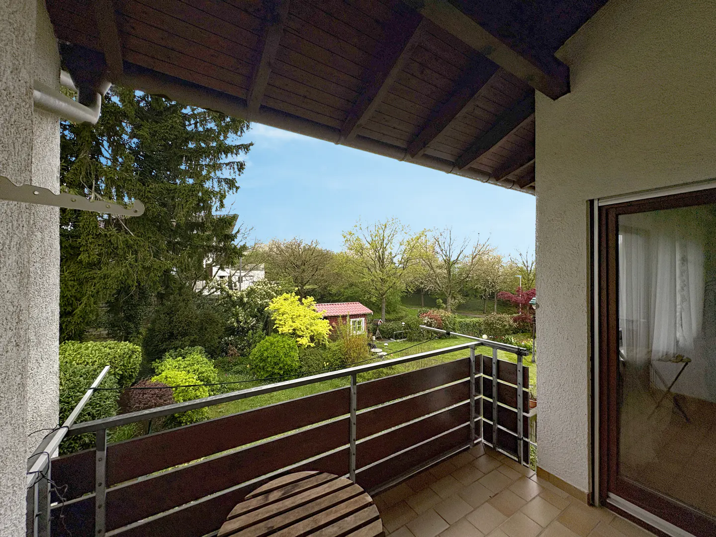 Balcony view with a small round table, metal railing, and a garden with a red shed in the background.