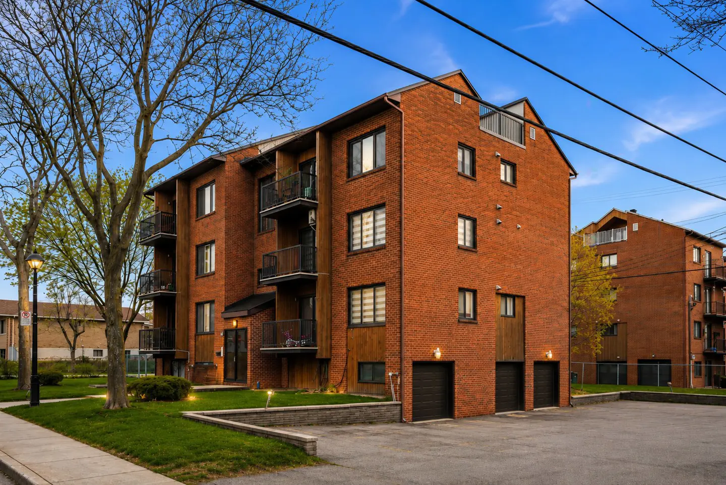 A three-story brick apartment building with black balconies and garage doors under a blue sky.
