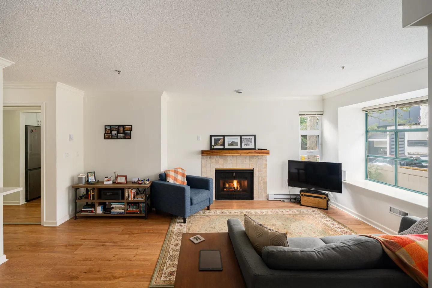Living room with hardwood floors, a fireplace with a wood mantel, and a blue armchair. A gray sofa faces the fireplace.