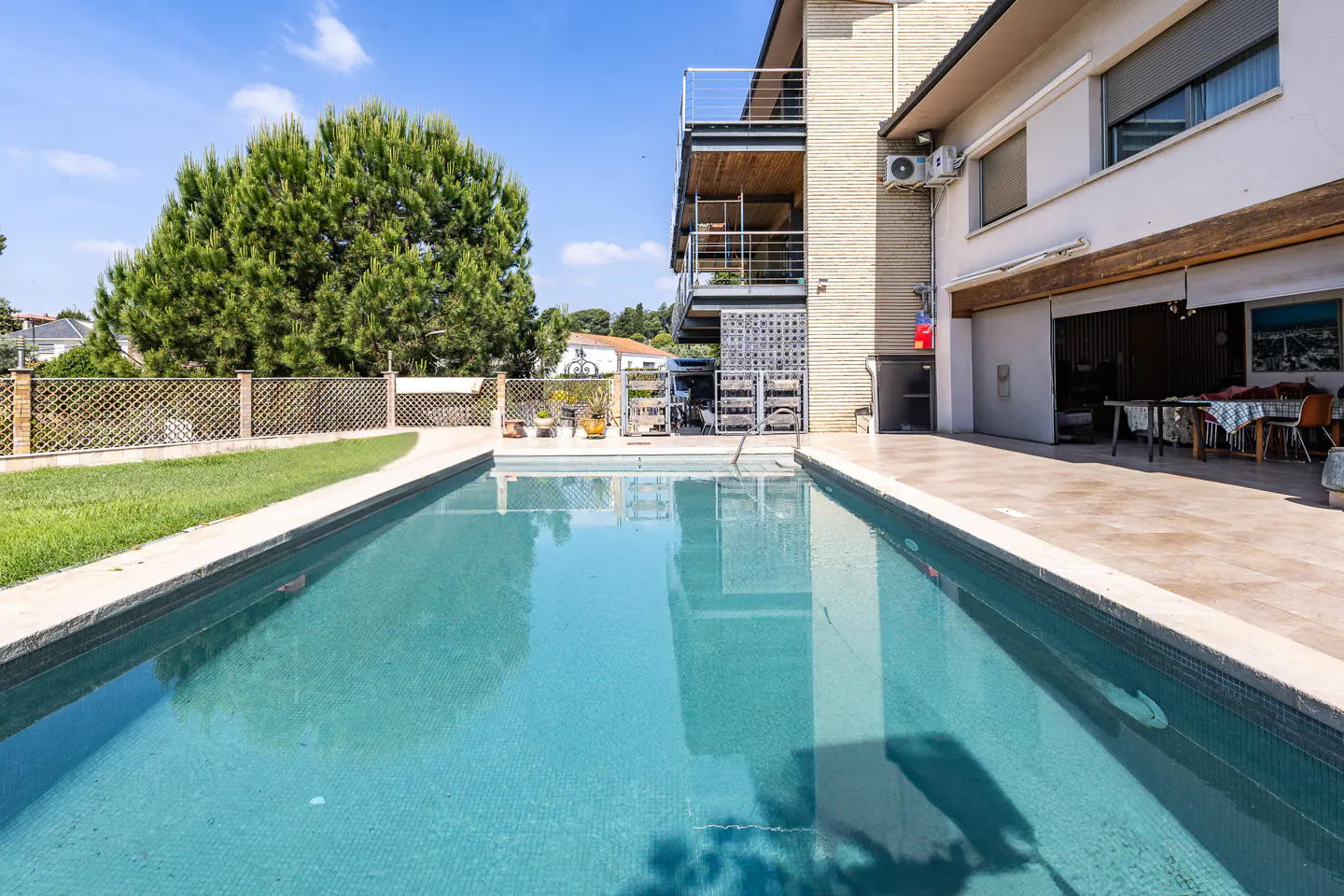 A rectangular pool with turquoise water sits in front of a two-story house with balconies and a patio.