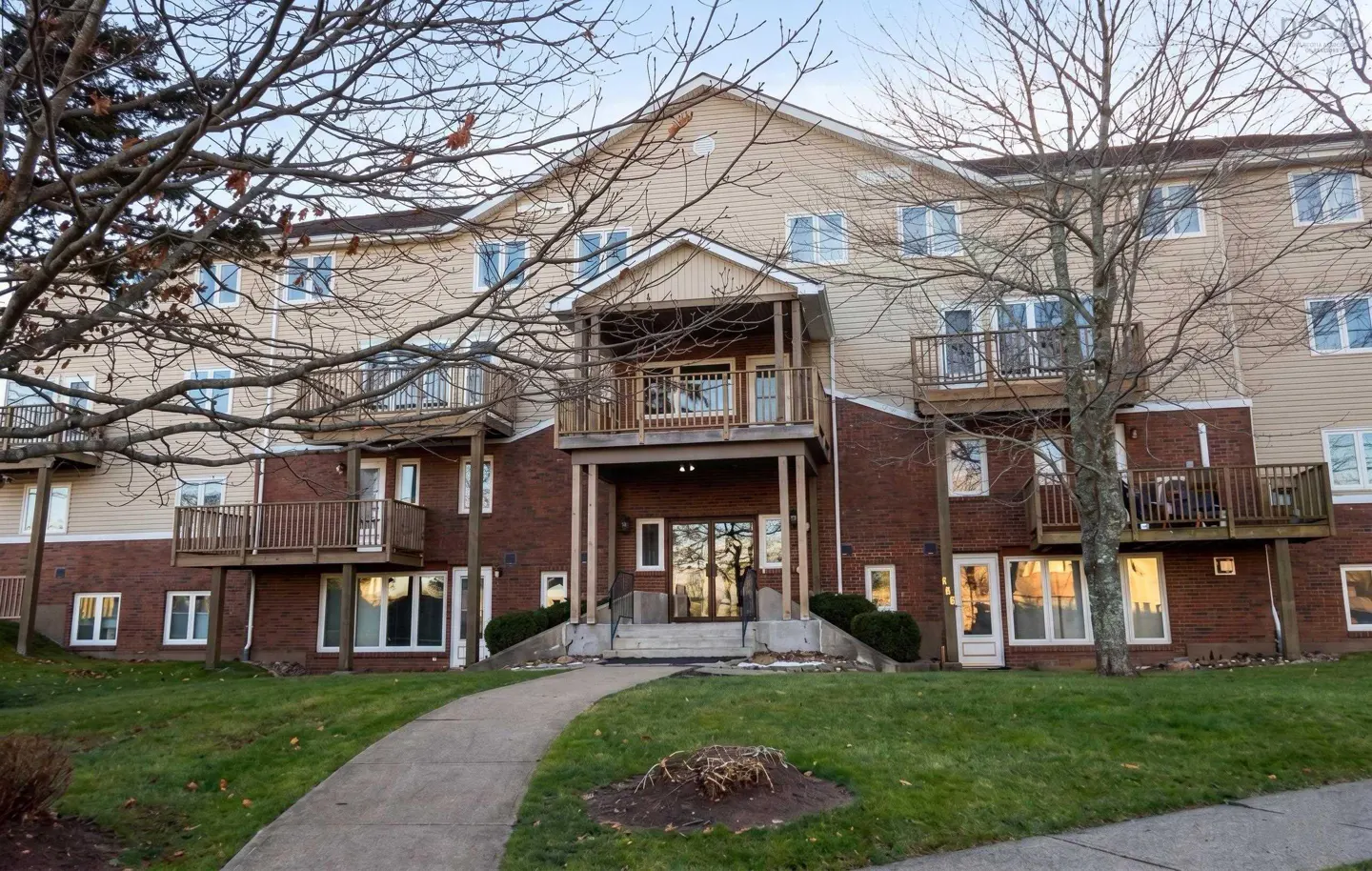 Three-story apartment building with brick and tan siding, balconies, and a walkway leading to the entrance.