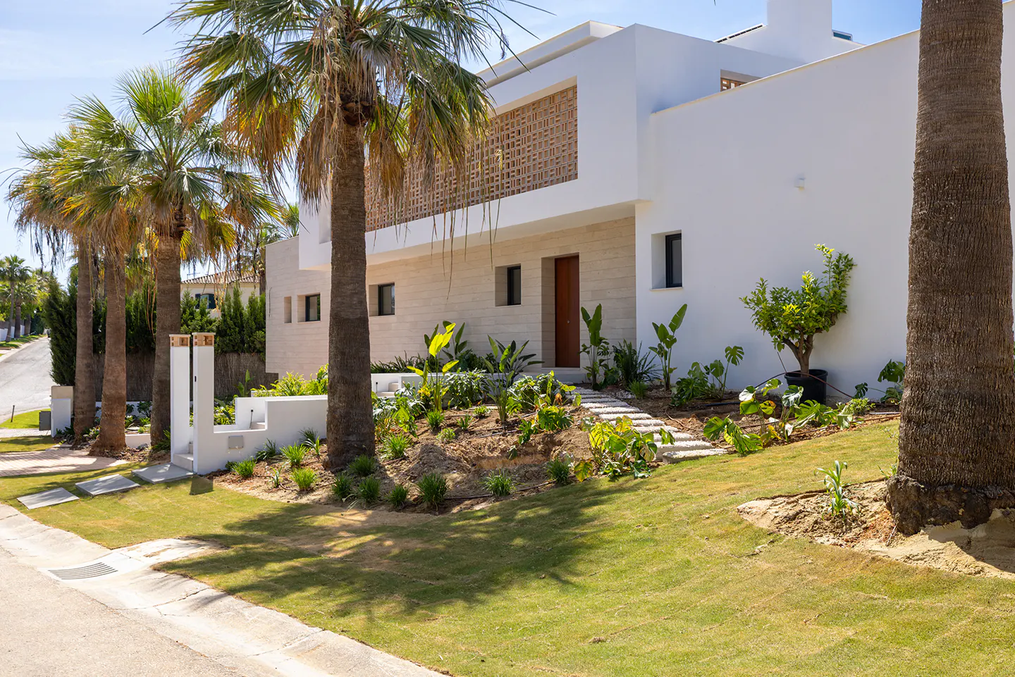 Modern white house with palm trees. A stone path leads to a brown door. A decorative lattice covers a window.