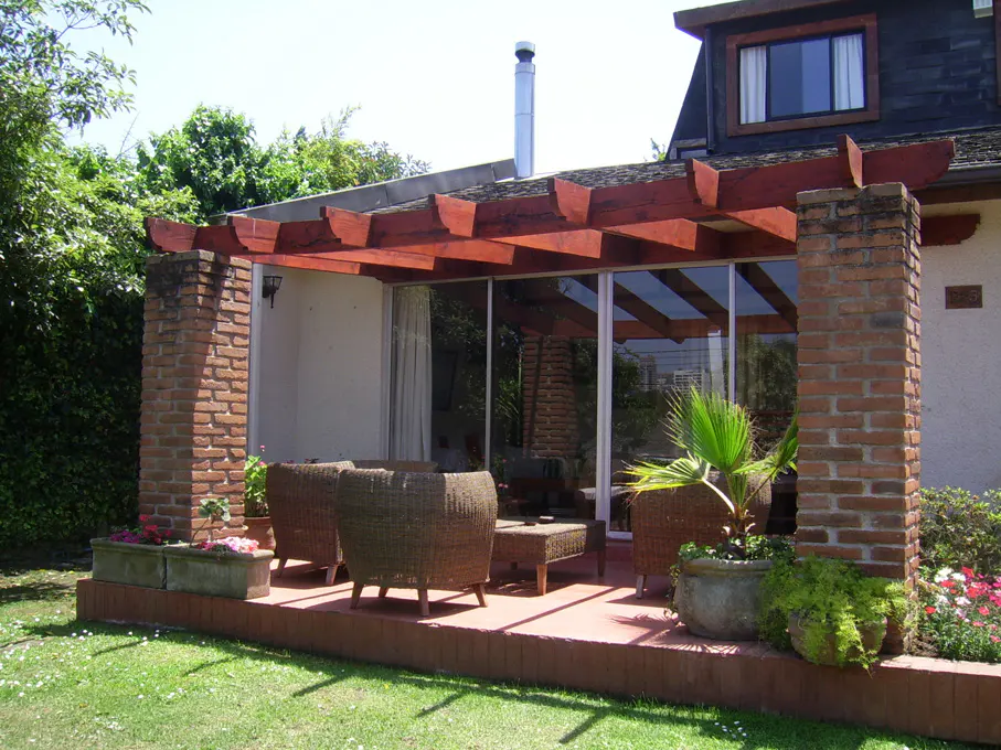 Outdoor patio with wicker furniture, brick columns, and a wood pergola. Green lawn and plants surround the patio.
