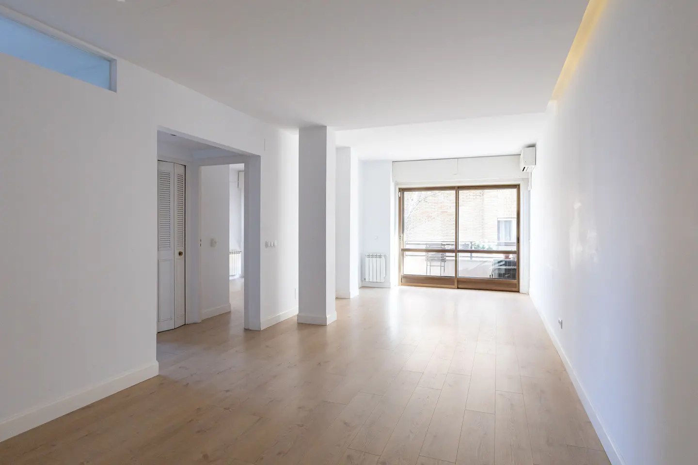 Bright, empty room with light wood floors and white walls. A large sliding glass door leads to a balcony.