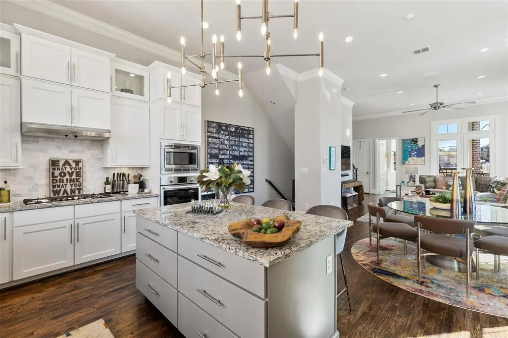 Open-concept kitchen with white cabinets, granite countertops, and a gray island. A dining area and living room are visible in the background.