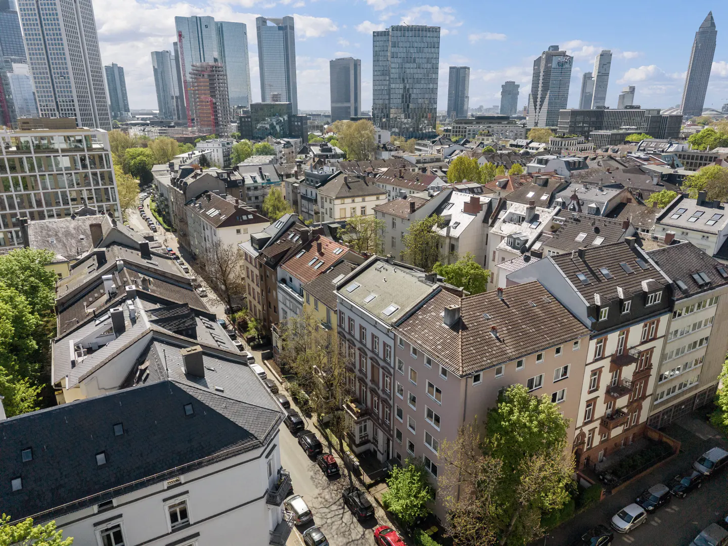 Cityscape view of Frankfurt, Germany, featuring residential buildings and modern skyscrapers under a blue sky with scattered clouds.