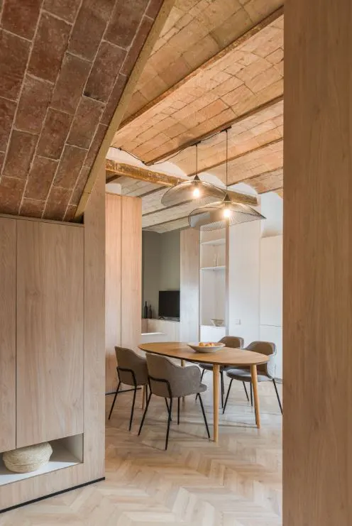 Interior view of a dining room with a brick ceiling, wood cabinets, and herringbone wood floors. A table and chairs are visible.