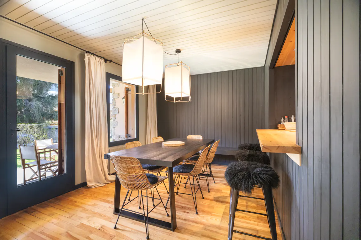 Dining room with wood floors, a dark wood table with wicker chairs, and two square white pendant lights. A bar with stools is on the right.