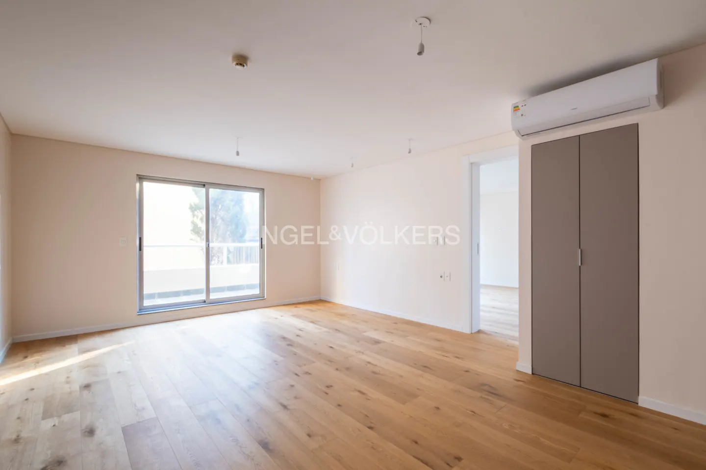 An empty, bright room with light wood floors, a sliding glass door, and a gray closet with an air conditioner above it.