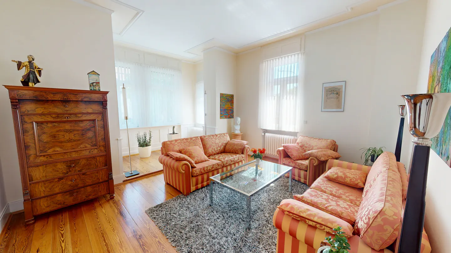 Living room with orange striped sofas, glass table on gray rug, and wooden cabinet on hardwood floor.