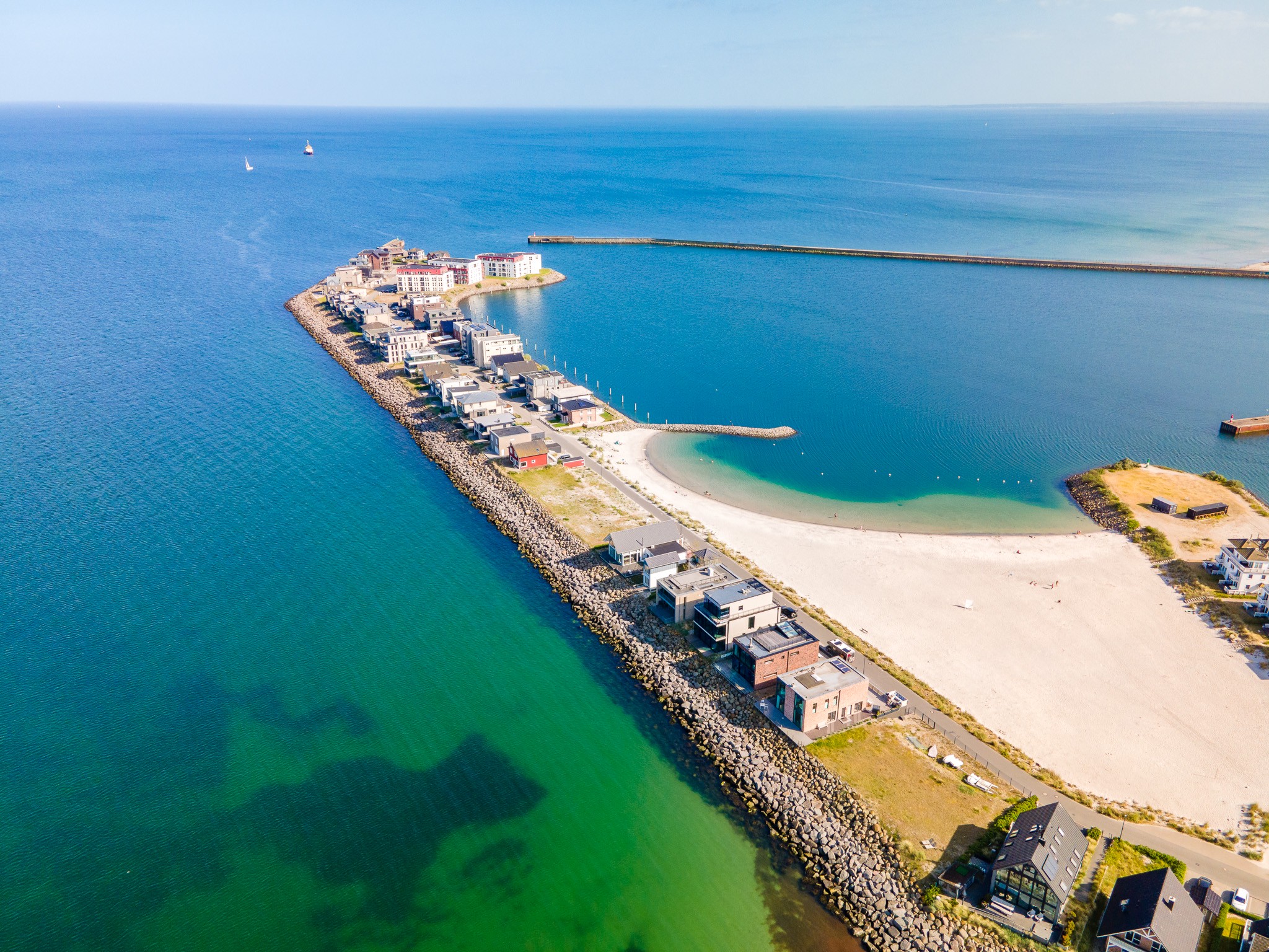 Aerial view of modern homes along a narrow peninsula with a sandy beach and blue ocean. [AI-generated text]