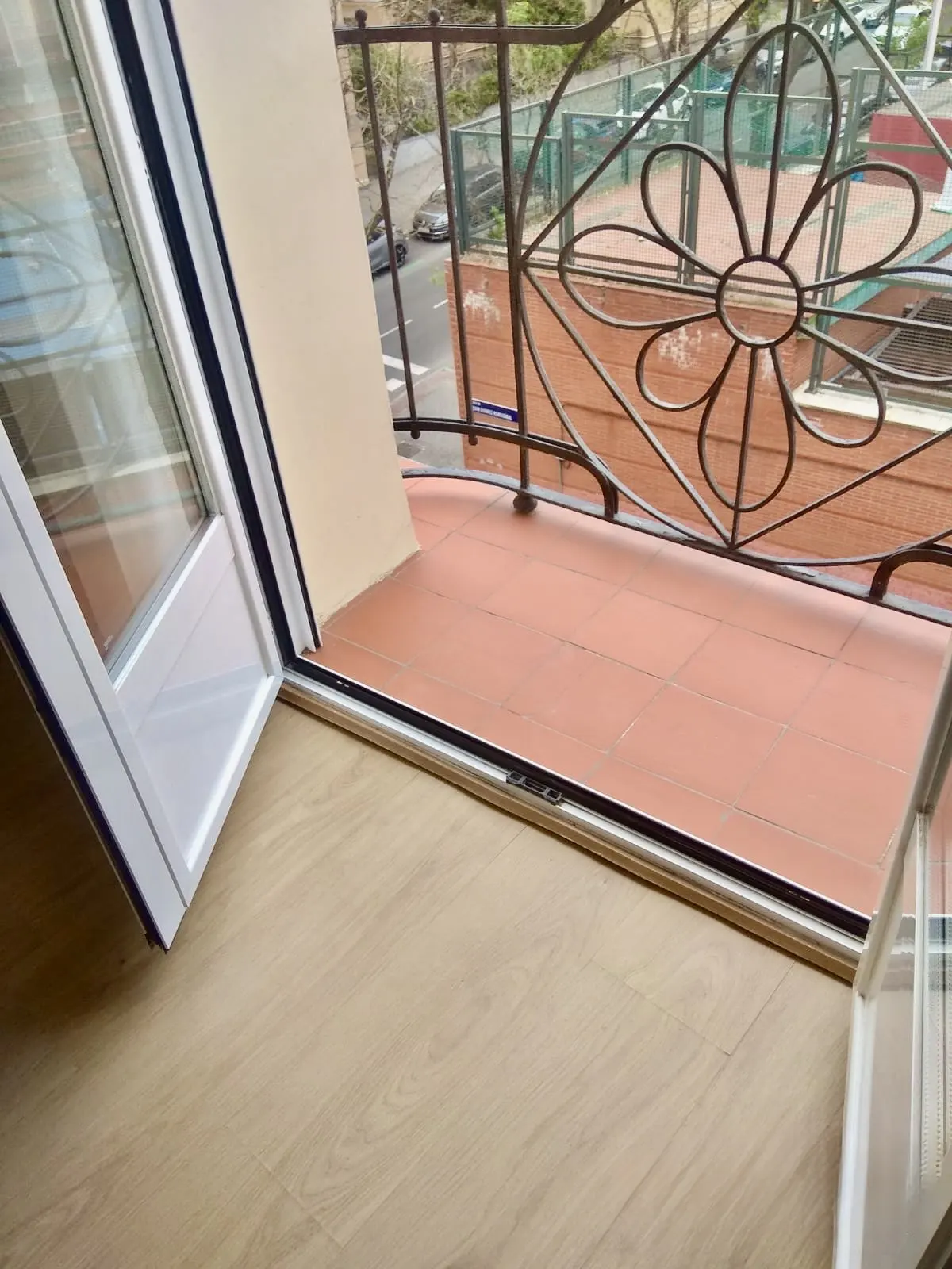 Open white patio door leads to a balcony with brown tile and decorative wrought iron railing.